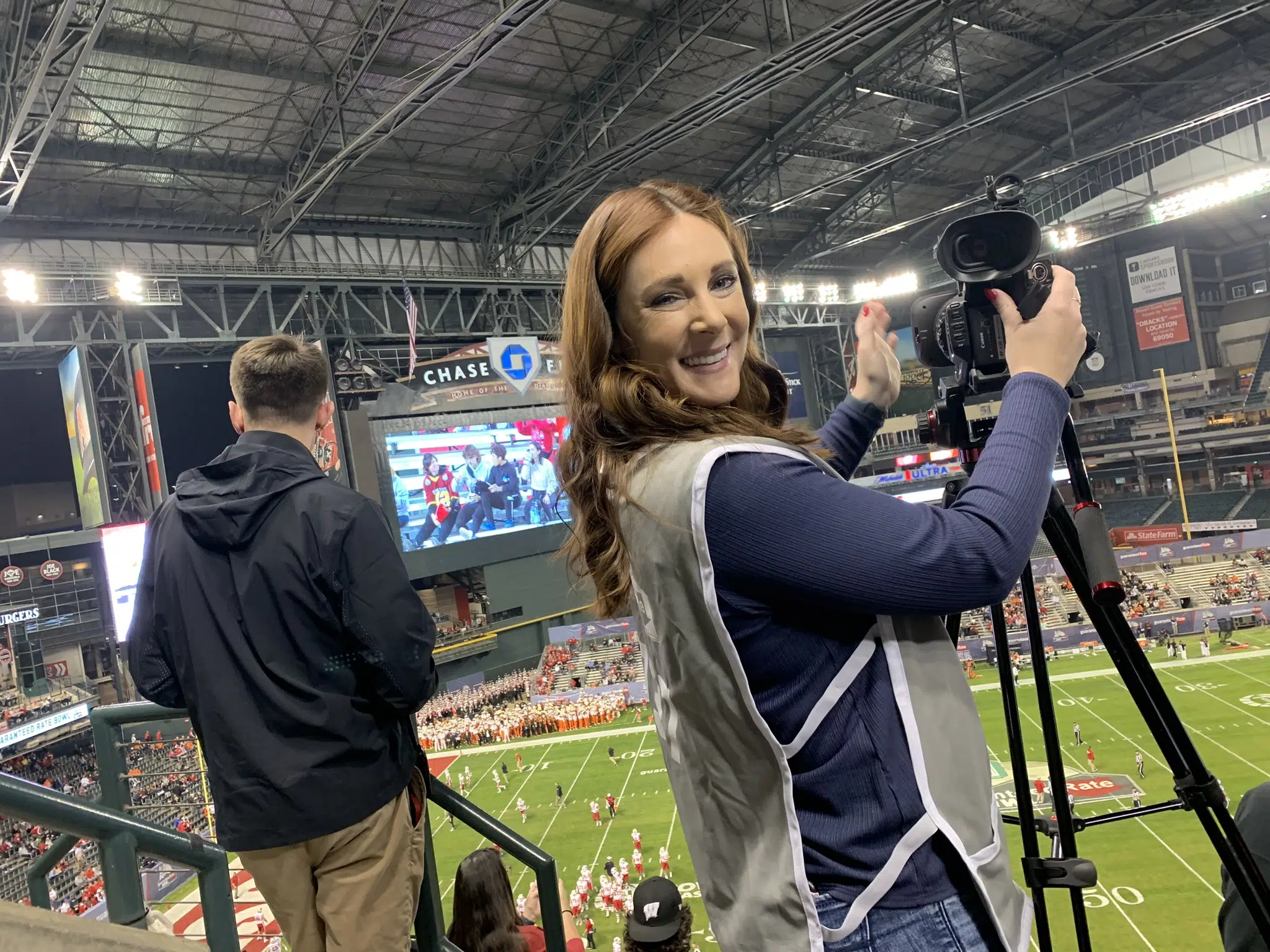 Camerawoman smiling next to camera at college football bowl game at Chase Field